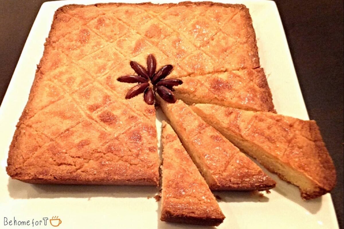 "A golden-brown, moist butter cake displayed on a white plate, cut into triangular slices. The cake has a crisscross pattern on the surface, and an anise star is placed in the center for decoration, enhancing the presentation.