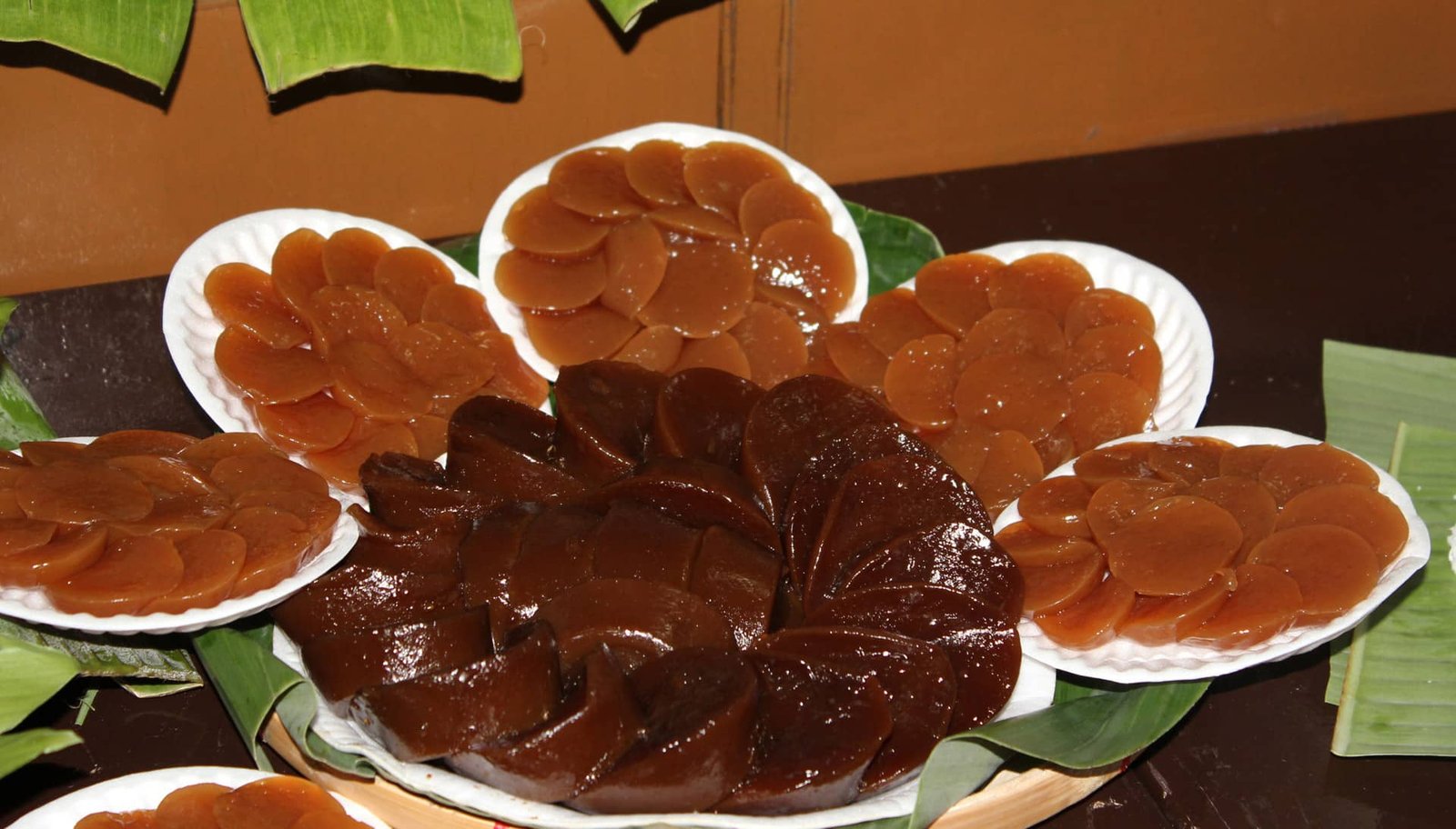 The image displays Pandan Kutsinta, a traditional Filipino rice cake made from glutinous rice flour and flavored with pandan. The brown, jelly-like rounds are arranged neatly on plates, showcasing their smooth, glossy texture. Typically served with grated coconut, these kutsinta are a favorite snack or dessert.