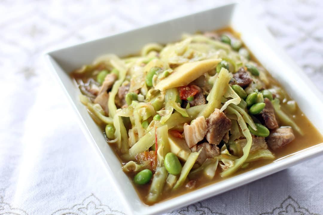 A vibrant bowl of Pinalatik Na Malunggay with Tulingan, showcasing a colorful medley of fresh malunggay leaves, tender slices of tulingan (mackerel), and savory vegetables. The dish is served in a light, flavorful broth, capturing the essence of Filipino home-cooked meals. The presentation highlights the hearty ingredients, including green beans and other fresh elements, in a white square dish.