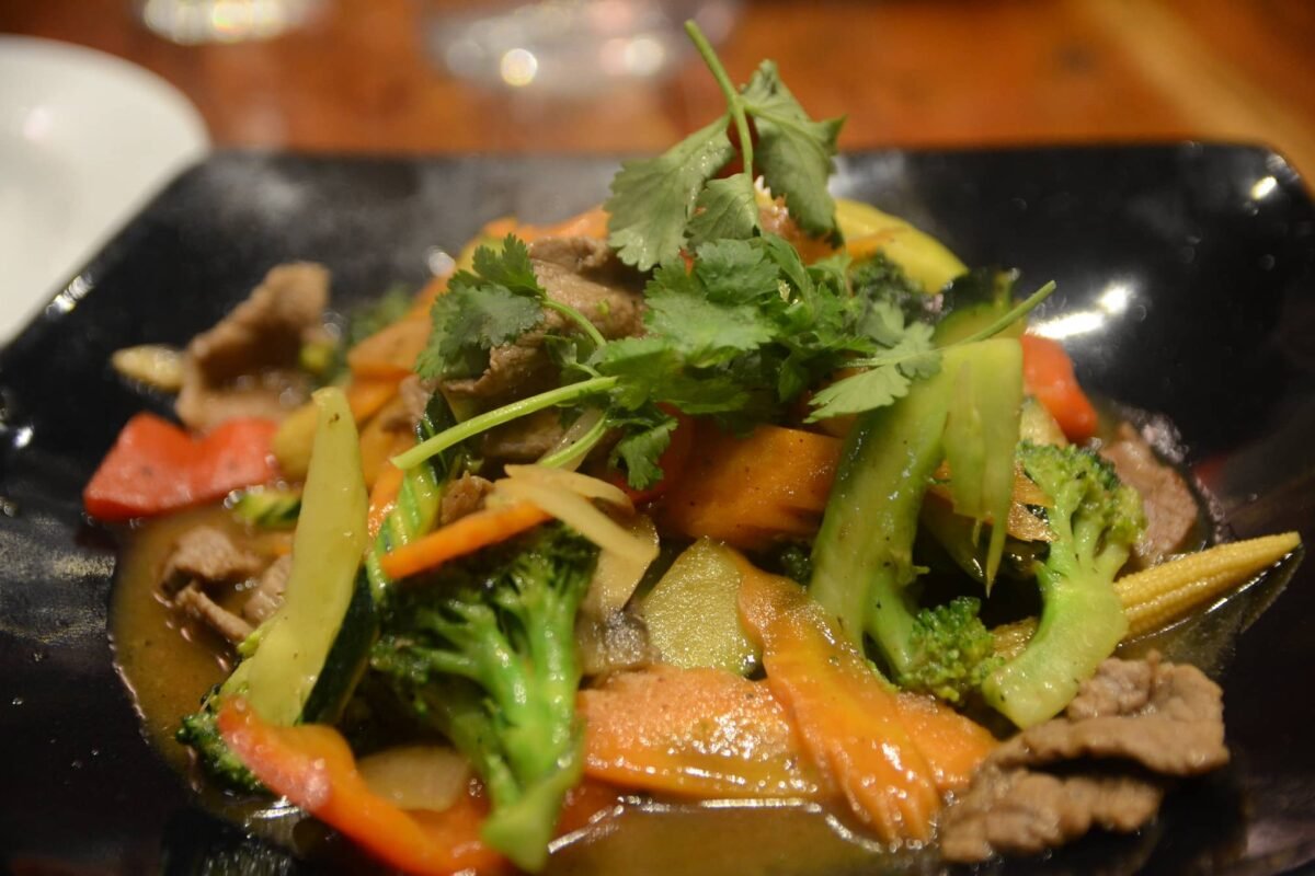 Close-up of a dish of Pork Ampalaya with Oyster Sauce, featuring tender slices of pork, ampalaya (bitter melon), and assorted vegetables like bell peppers, carrots, broccoli, and baby corn, garnished with fresh cilantro. The dish is served on a dark plate, showcasing a rich, savory oyster sauce glaze.