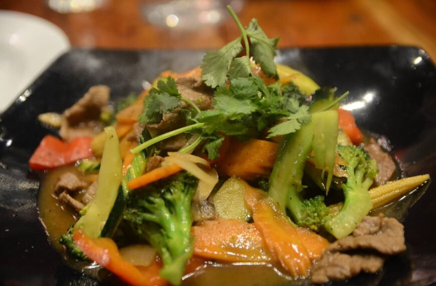 Close-up of a dish of Pork Ampalaya with Oyster Sauce, featuring tender slices of pork, ampalaya (bitter melon), and assorted vegetables like bell peppers, carrots, broccoli, and baby corn, garnished with fresh cilantro. The dish is served on a dark plate, showcasing a rich, savory oyster sauce glaze.