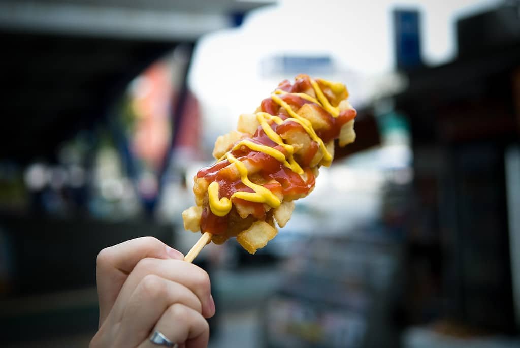 A potato cheese stick topped with ketchup and mustard on a skewer.