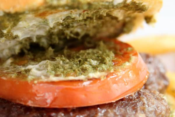 Close-up of a Puso ng Saging Gawing Burger Patty, featuring a juicy tomato slice on top of a banana heart patty, with a layer of green pesto sauce on the bun. The burger showcases a unique fusion of Filipino flavors, combining the tender texture of banana heart with the freshness of tomato and the rich taste of pesto.