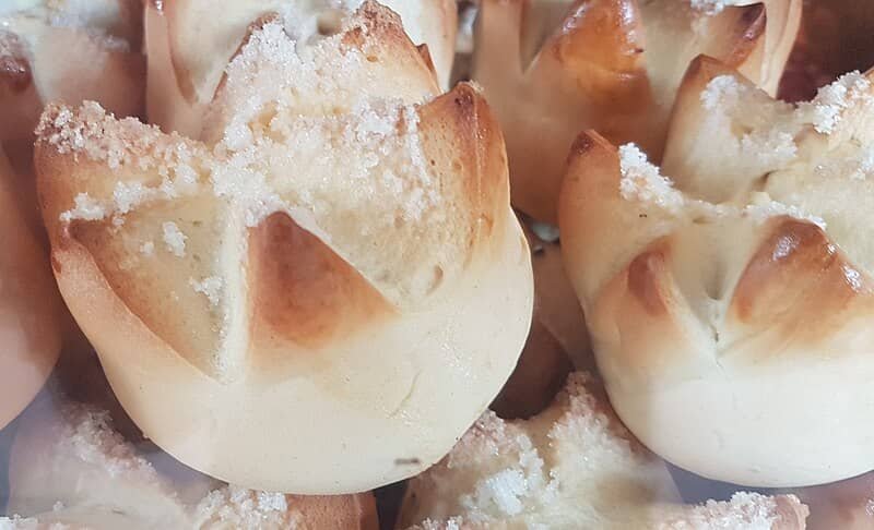 Close-up of freshly baked Putok bread, also known as star bread, with a cracked top and a sprinkling of sugar. These Filipino buns are golden brown, slightly sweet, and have a signature "exploded" top, making them a perfect snack or breakfast treat.