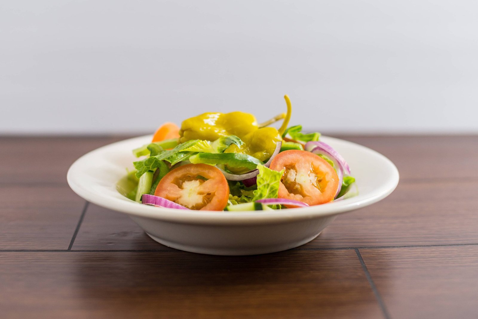 A fresh and vibrant vegetable salad featuring sliced sibuyas (onions), crisp lettuce, tomatoes, and green peppers. The salad is served in a white bowl, showcasing the colorful mix of ingredients, perfect for a healthy and light meal.