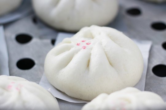 A close-up of freshly steamed Siopao Asado, a Filipino-Chinese bun filled with savory sweet pork, sitting on parchment paper ready to be served.