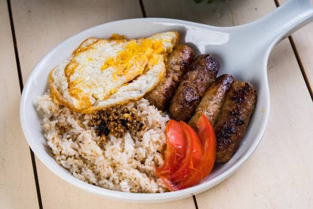 A hearty Filipino breakfast plate featuring skinless longganisa sausages, garlic fried rice, a sunny-side-up egg, and fresh tomato slices, highlighting a traditional skinless longganisa recipe.