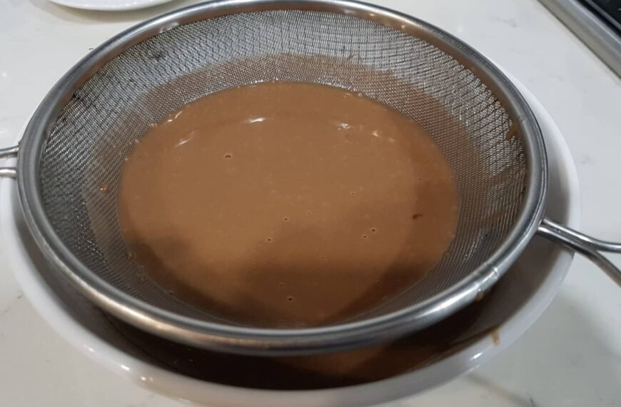 The image seems to depict a chocolate mixture being strained, which might be a step in preparing a dessert, possibly related to a dish like "Steam Milo Cheese." Milo is a popular chocolate malt powder often used in Filipino desserts.