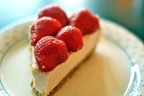 A slice of strawberry cheesecake topped with fresh strawberries on a plate.