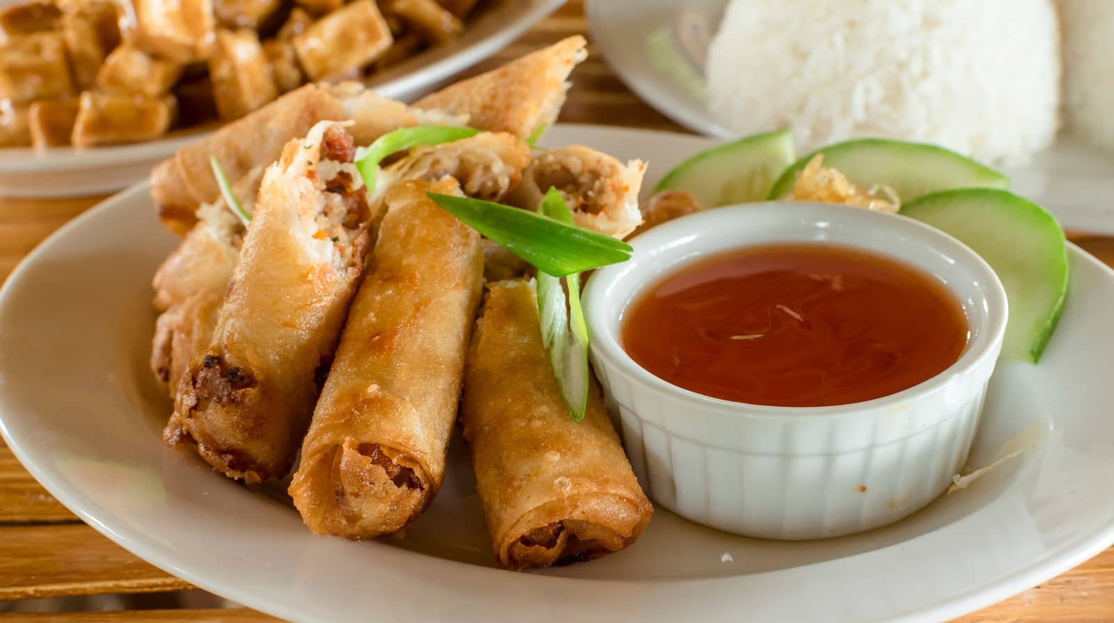 A plate of golden spring rolls served with a tangy, homemade sweet and sour sauce, accompanied by cucumber slices, perfect for pairing with your Easy Homemade Sweet and Sour Sauce Recipe.