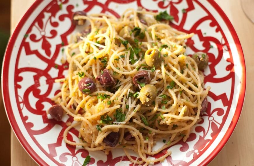 The image shows a plate of Tuyo Pasta, a Filipino dish made with spaghetti, topped with olives, garlic, and dried fish (tuyo), garnished with fresh parsley.