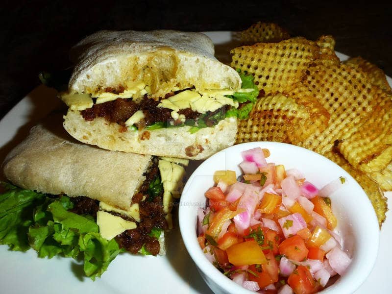 A sandwich filled with savory Vigan Longganisa, lettuce, and melted cheese, served with a side of crispy waffle fries and a small bowl of diced tomato and onion salsa. This Vigan Longganisa Recipe showcases the rich flavors of the famous Filipino sausage in a modern dish.