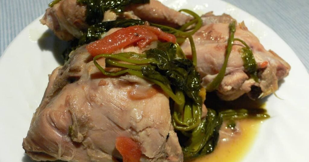 A close-up of tender chicken pieces simmered in a flavorful Bicol Express sauce, garnished with fresh greens and tomatoes, served on a white plate.