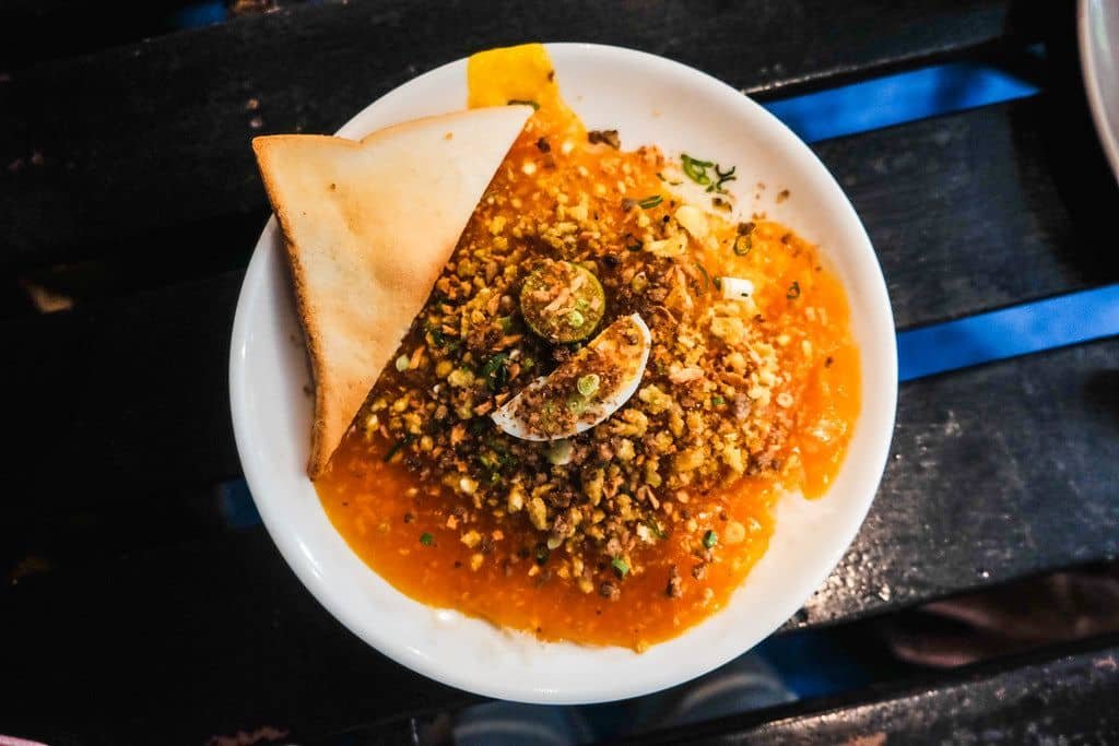 A plate of Cuchinta Tahada topped with crushed nuts, a slice of boiled egg, and finely chopped herbs. The dish is garnished with a triangle of toasted bread, adding a crispy texture to the smooth and savory base, creating a visually appealing and flavorful Filipino delicacy.