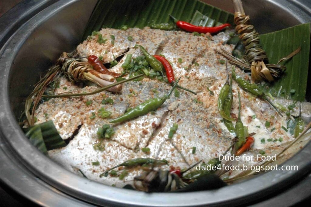 The image showcases Pakfry, a famous dish from Davao made from fried fish, typically tuna or milkfish, prepared in a unique way. The fish is first fried and then simmered in a mixture of vinegar, garlic, and spices, often served with a garnish of chilis and lemongrass. The dish is known for its rich flavor and combination of crispy and tangy elements, making it a beloved part of Davao's culinary offerings.
